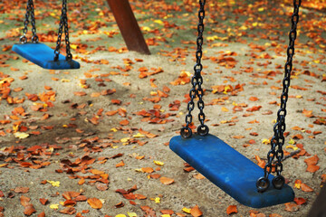two empty blue plastic swings on thick metal chains against the background of orange fallen leaves in the Park in autumn