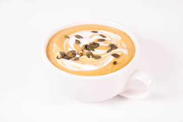 Pumpkin soup decorated with cream and pumpkin seeds in a bowl on a white background