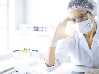 Naklejka premium Professional female scientist in protective eyeglasses researching tube with reagents in sunny laboratory. Medicine and science researching