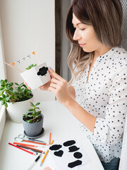 Smiling woman shows handmade decorations for Halloween. DIY flags and Boo! sticker on flowerpot...