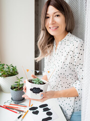 Smiling woman shows handmade decorations for Halloween. DIY flags and Boo! sticker on flowerpot...