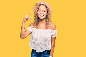 Beautiful caucasian woman wearing summer hat smiling and confident gesturing with hand doing small size sign with fingers looking and the camera. measure concept.