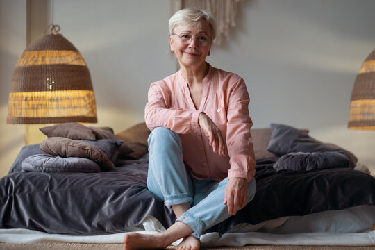 Senior Woman Sitting At Home On Bed Smiling.