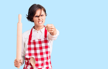 Beautiful young woman with short hair wearing professional baker apron holding kneading roll annoyed and frustrated shouting with anger, yelling crazy with anger and hand raised