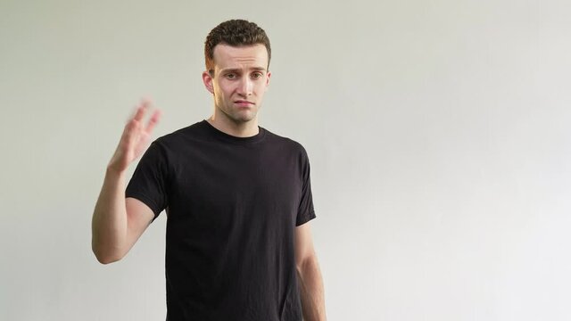 Dislike gesture. Disgusted man. Bad idea. Refusal sign. Skeptic annoyed guy in black t-shirt rejecting offer with thumb down go away no signal isolated on light neutral empty space background.