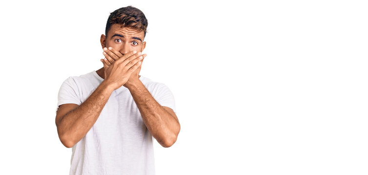 Young hispanic man wearing casual white tshirt shocked covering mouth with hands for mistake. secret concept.