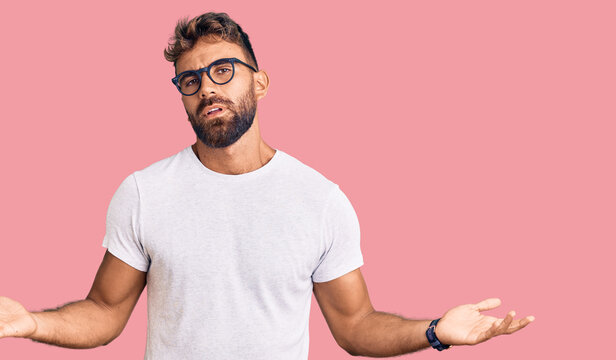 Young hispanic man wearing casual clothes and glasses clueless and confused with open arms, no idea concept.