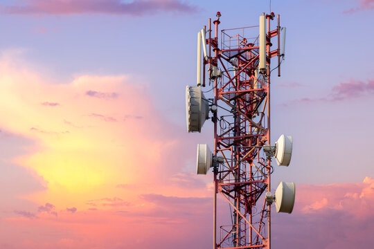 Telecommunication tower with antennas against beautiful colorful sky at sunset or dawn with pink clouds background.