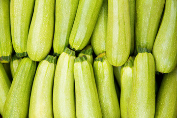 Fresh green zucchini are laid out in a row on the counter of the vegetable market.