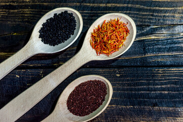Indian spices in wooden spoons. On a wooden burnt background in the village style, saffron, black cumin, sumac. Culinary background with the ability to insert a small piece of text