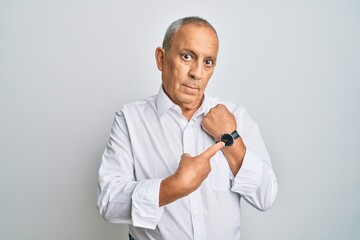 Handsome senior man wearing casual white shirt in hurry pointing to watch time, impatience, looking at the camera with relaxed expression