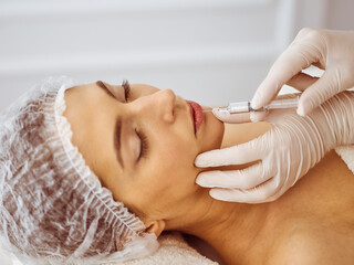 Beautician doing beauty procedure with syringe to face of young brunette woman. Cosmetic medicine and surgery, beauty injections