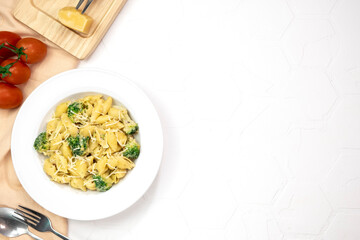 Pasta with green vegetables, broccoli, melted cheese and creamy sauce in white bowl on white table. 