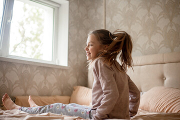 Female child lies on pillow in bed in bedroom at the motning. Girl enjoys bedtime.
