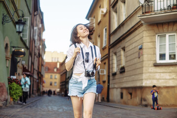 The girl in the black hat and sun glasses with photo camera on a road in an old european town.