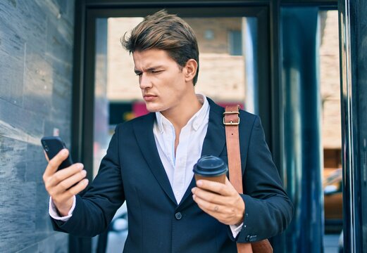 Young caucasian businessman with serious expression using smartphone and drinking coffee at the city.