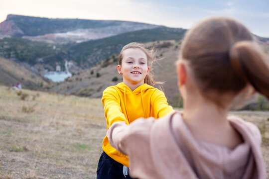 Two preteen girls traveler wearing yellow and biege hoodie walking  on top of the mountain landscape and looking to the sea