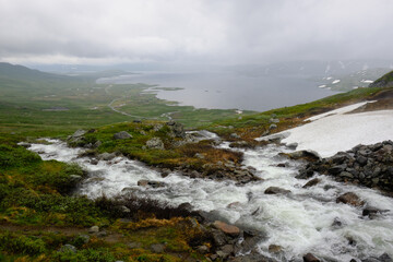 Fast-flowing mountain stream and snow on a Norwegian highland during a rainy summer day