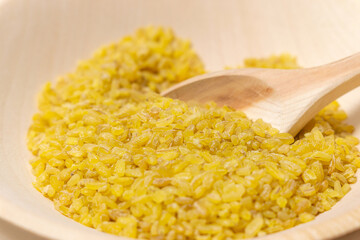 Raw bulgur in wooden bowl, close up shot. Healthy dietary vegan gluten free product.