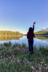 Girl Standing with Beautiful Scenery and wild flowers by the lake during a clear sunny evening in Canadian Nature. Taken near Whitehorse, Yukon, Canada.