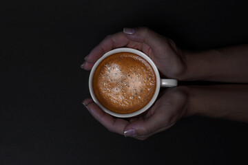 Female hands holding white cup of coffee with crema