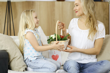 Obraz na płótnie Canvas Happy mother day. Child daughter congratulates mom and gives her basket of spring flowers and postcard with heart drawing. Family and childhood concepts
