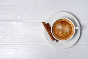 White cup of coffee with crema, cinnamon sticks on white wooden background