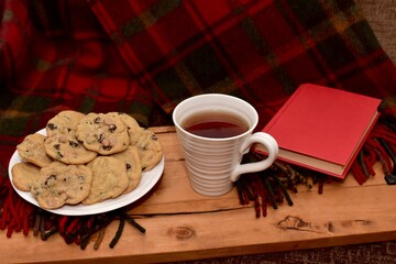 Fresh homemade warm comforting chocolate chip cookies ready to eat and enjoy with cozy mug of tea and relaxing with a book on a cold winter afternoon