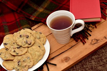 Fresh homemade warm comforting chocolate chip cookies ready to eat and enjoy with cozy mug of tea and relaxing with a book on a cold winter afternoon