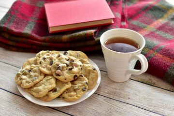 Fresh homemade warm comforting chocolate chip cookies ready to eat and enjoy with cozy mug of tea and relaxing with a book on a cold winter afternoon