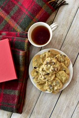 Fresh homemade warm comforting chocolate chip cookies ready to eat and enjoy with cozy mug of tea and relaxing with a book on a cold winter afternoon