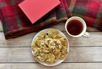 Fresh homemade warm comforting chocolate chip cookies ready to eat and enjoy with cozy mug of tea and relaxing with a book on a cold winter afternoon