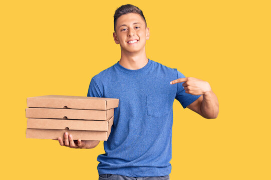 Young handsome hispanic man holding delivery pizza box pointing finger to one self smiling happy and proud