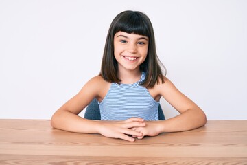 Young little girl with bang wearing casual clothes sitting on the table with a happy and cool smile on face. lucky person.