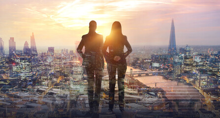 Two young woman looking at city of London at sunset. River Thames, embankment, business area of the City. London, UK