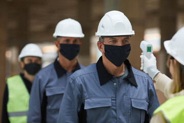 Close up of supervisor measuring temperature of workers with contactless thermometer at construction site, corona virus safety