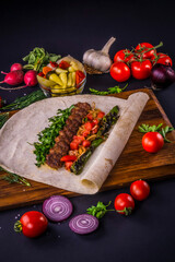 Turkish and Arabic Traditional Ramadan Adana Kebab Roll Wrap serving with vegatable, aubergine salad and hot pepper pickles on rustic wooden background. 