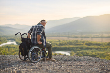 A young man getting up from a wheelchair on top of a mountain at sunrise. The invalid was healed.