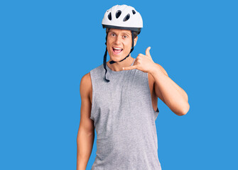 Young handsome man wearing bike helmet smiling doing phone gesture with hand and fingers like talking on the telephone. communicating concepts.