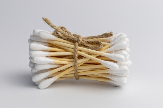 Eco-friendly wooden cotton ear sticks or ear swabs made without plastic connected with roap with white background. Sustainability and recycling worldwide problems.