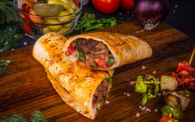 Turkish and Arabic Traditional Ramadan Adana Kebab Roll Wrap serving with yogurt  aubergine salad and hot pepper pickles on rustic wooden background.