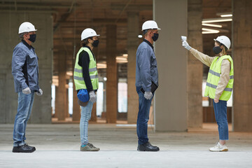 Side view full length of female supervisor measuring temperature of workers with contactless...