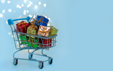 Small decorative basket with multi-colored gift boxes on a blue background. Online sales and shopping concept. Winter Christmas holiday sales, seasonal sales, Christmas, Black Friday, discounts.