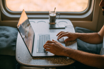 Male hands with a laptop on the table in the train. Close-up.