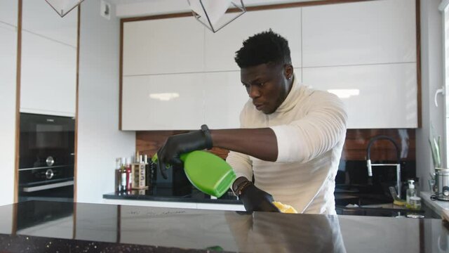 Black man spraying kitchen surface with disinfectant . Germaphobe doing domestic housework. High quality 4k footage