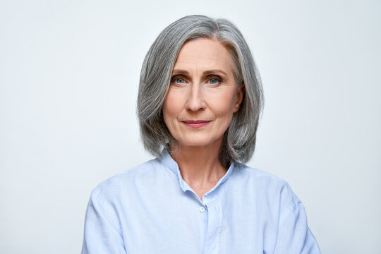 Confident beautiful mature business woman standing isolated on white background. Older senior businesswoman, 60s grey haired lady professional looking at camera, close up face headshot portrait.
