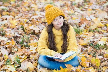 Small child read book with thoughtful look sitting on autumn leaves outdoors, imagination