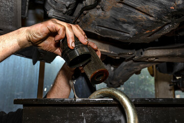 Car mechanic holding old worn out oil filter, hands dirty with black oil.