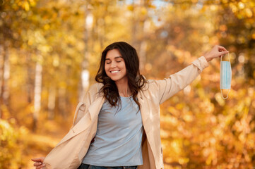 Young lady holding antiviral face mask in her hand and feeling happy over end of coronavirus...