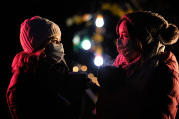 Frauen mit Maske auf einem Weihnachtsmarkt trinken Glühwein oder heiße Schokolade